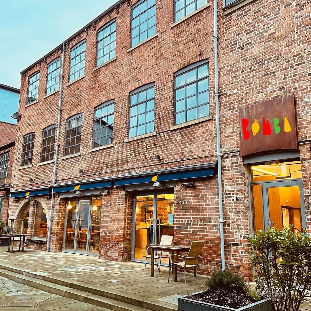 Exterior view of Bomba Paella, a brick building with large windows and a colorful sign above the entrance.