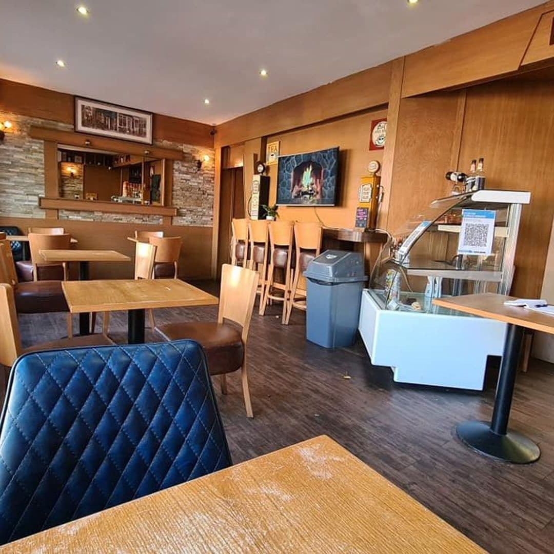 Interior view of Cafe Fraiche with wooden tables and chairs, a blue upholstered booth, a counter with bar stools, and warm lighting.