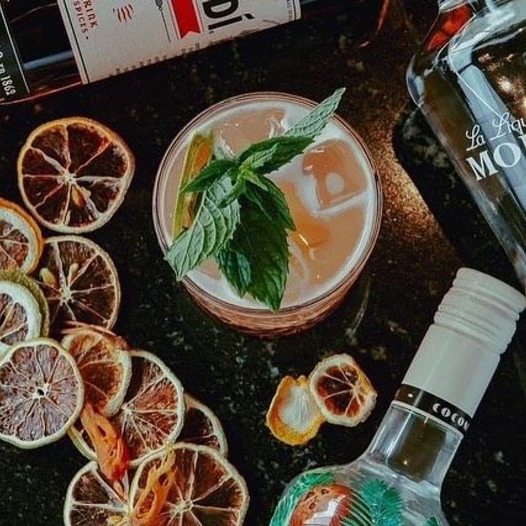 Refreshing cocktail garnished with mint at Dastaan, surrounded by dried citrus slices and a bottle of La Maison Coloniale spirit.