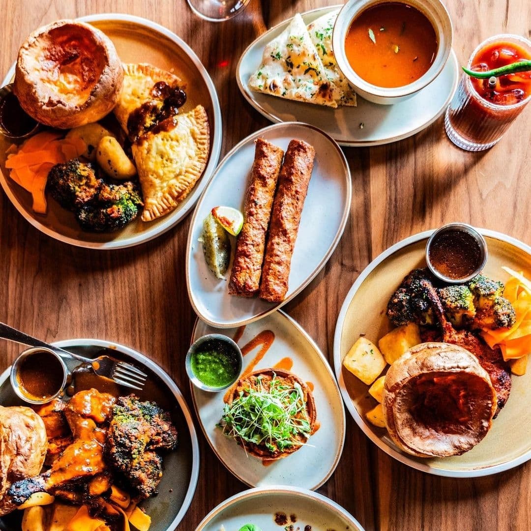 Assorted traditional dishes served at Dastaan, featuring savory pies, grilled kebabs, seasoned vegetables, and dipping sauces on wooden table.