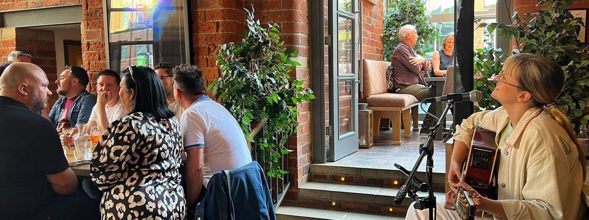 Patrons enjoying a lively atmosphere at Farrands Bar with indoor seating, exposed brick walls, and a live musician playing the guitar.