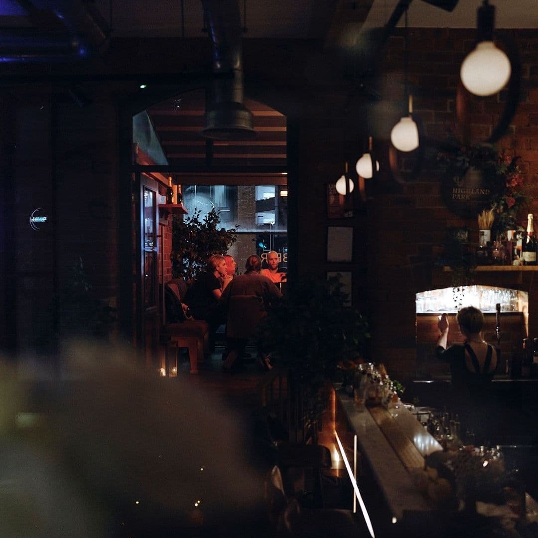 Cozy evening ambiance at Farrands Bar with patrons enjoying drinks and conversation, warm lighting, and rustic brick wall decor.