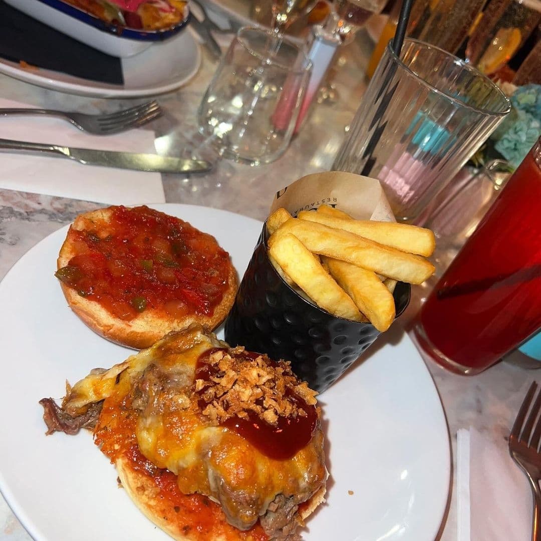 Gourmet burger with melted cheese and crispy onions, served with a side of fries and tomato-topped bread at Fleur Restaurant and Bar.