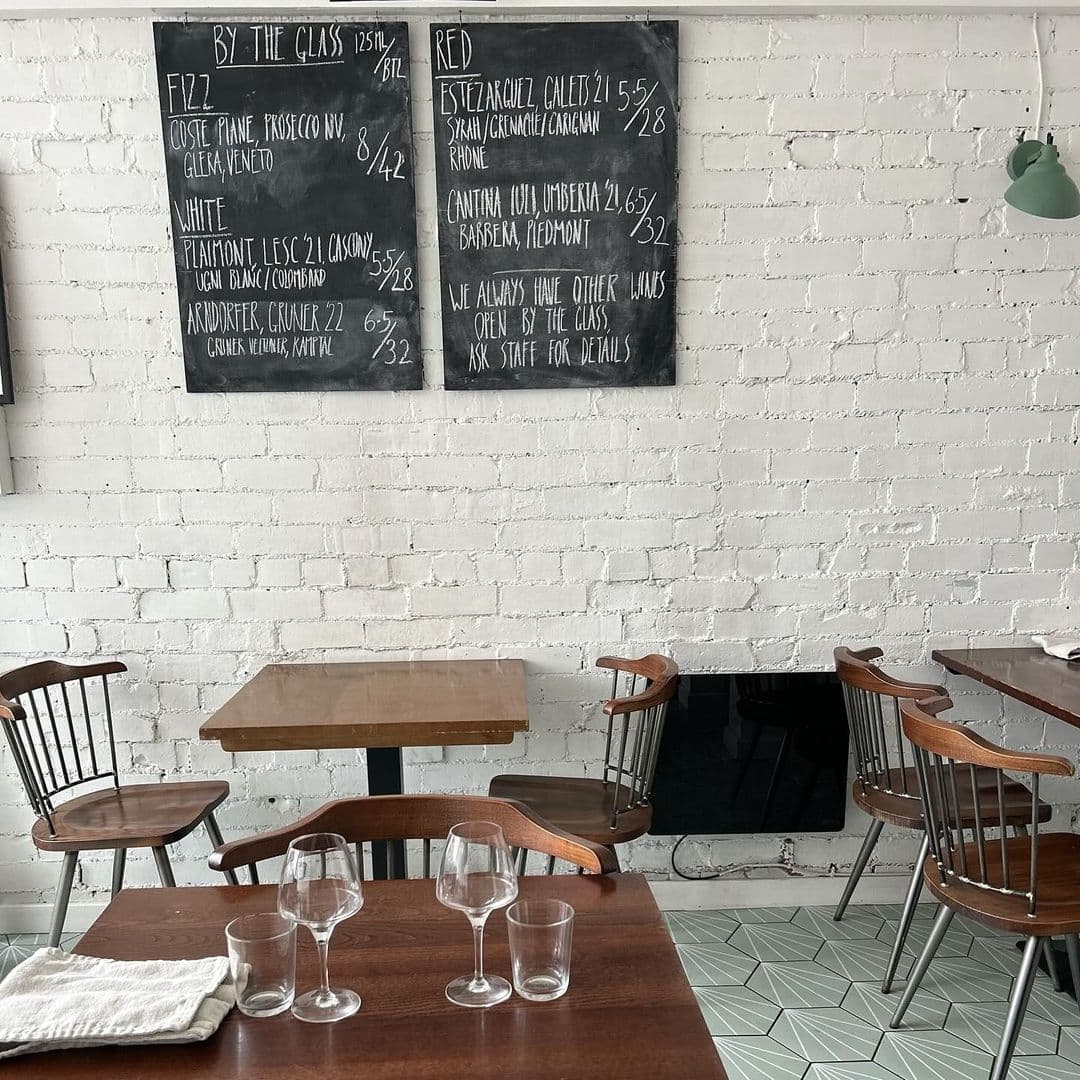 Interior of Hern restaurant with wooden tables and chairs, white brick walls, and a blackboard menu featuring wine selections.