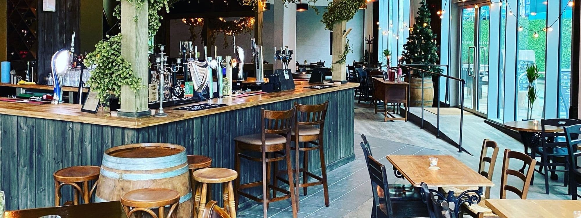 Interior of Hoist House featuring a cozy bar with taps and stools, wooden tables, festive decorations, and a welcoming atmosphere for visitors.
