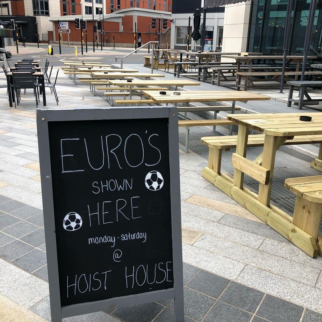 Outdoor seating area at Hoist House with wooden picnic tables and a chalkboard sign advertising Euros football matches shown Monday to Saturday.