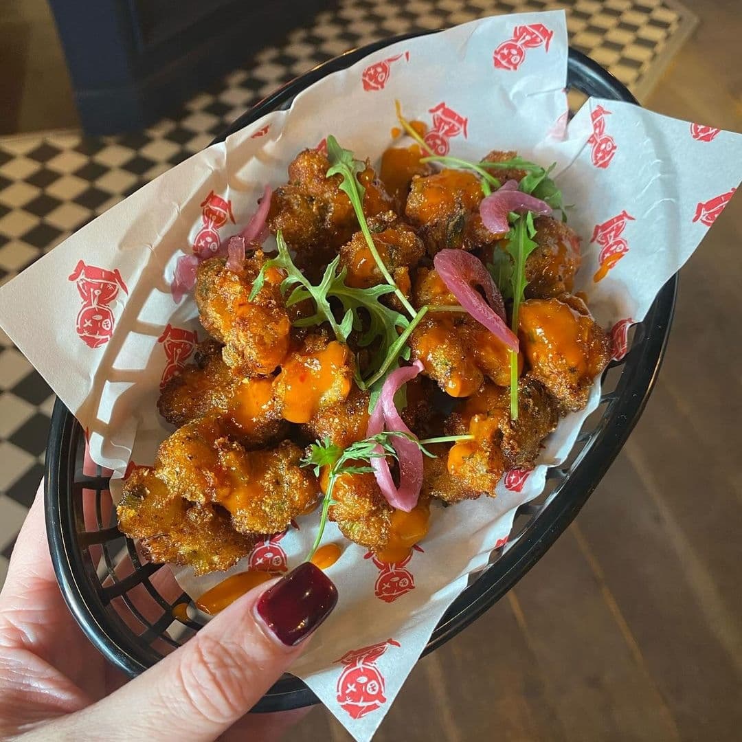 A person holding a basket of buffalo cauliflower bites garnished with fresh herbs and pickled onions at Hyde Park Pub.