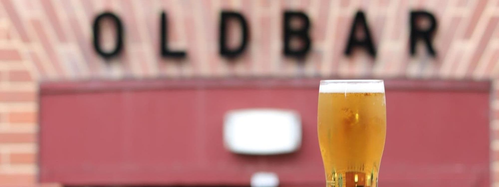 Pint of beer in focus with the blurred sign reading 'OLDBAR' in the background at Old Bar – Leeds Uni.