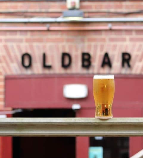 A refreshing pint of beer on a wooden railing with the sign 'OLDBAR' in the background at Old Bar – Leeds Uni.