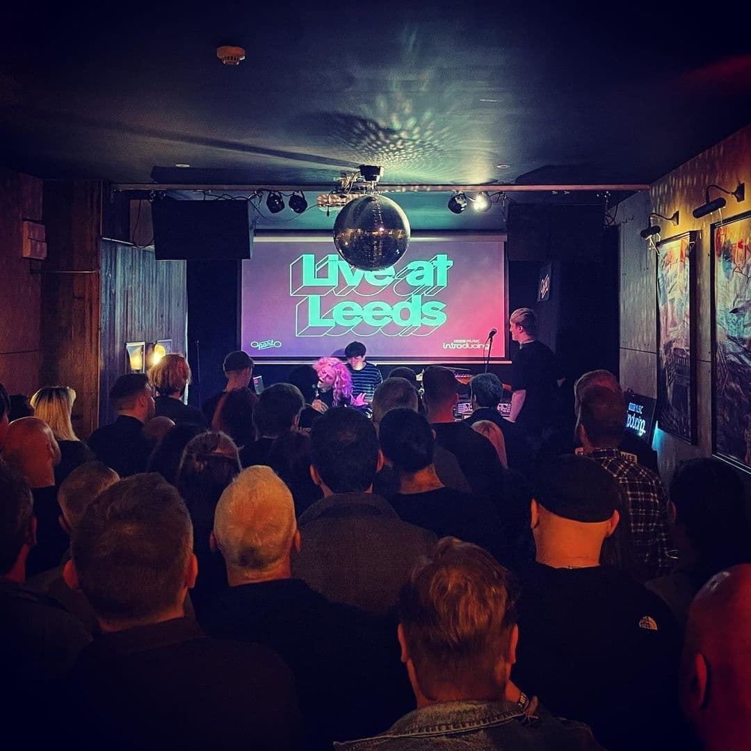 Crowd of people attending a live music event at Oporto, with a stage featuring the text "Live at Leeds" and a performer under a disco ball.