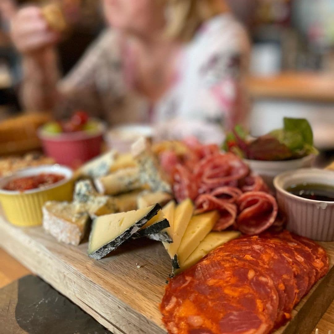 "Charcuterie board with a selection of cheeses and cured meats at Out of the Woods, with a blurred background of a person dining."