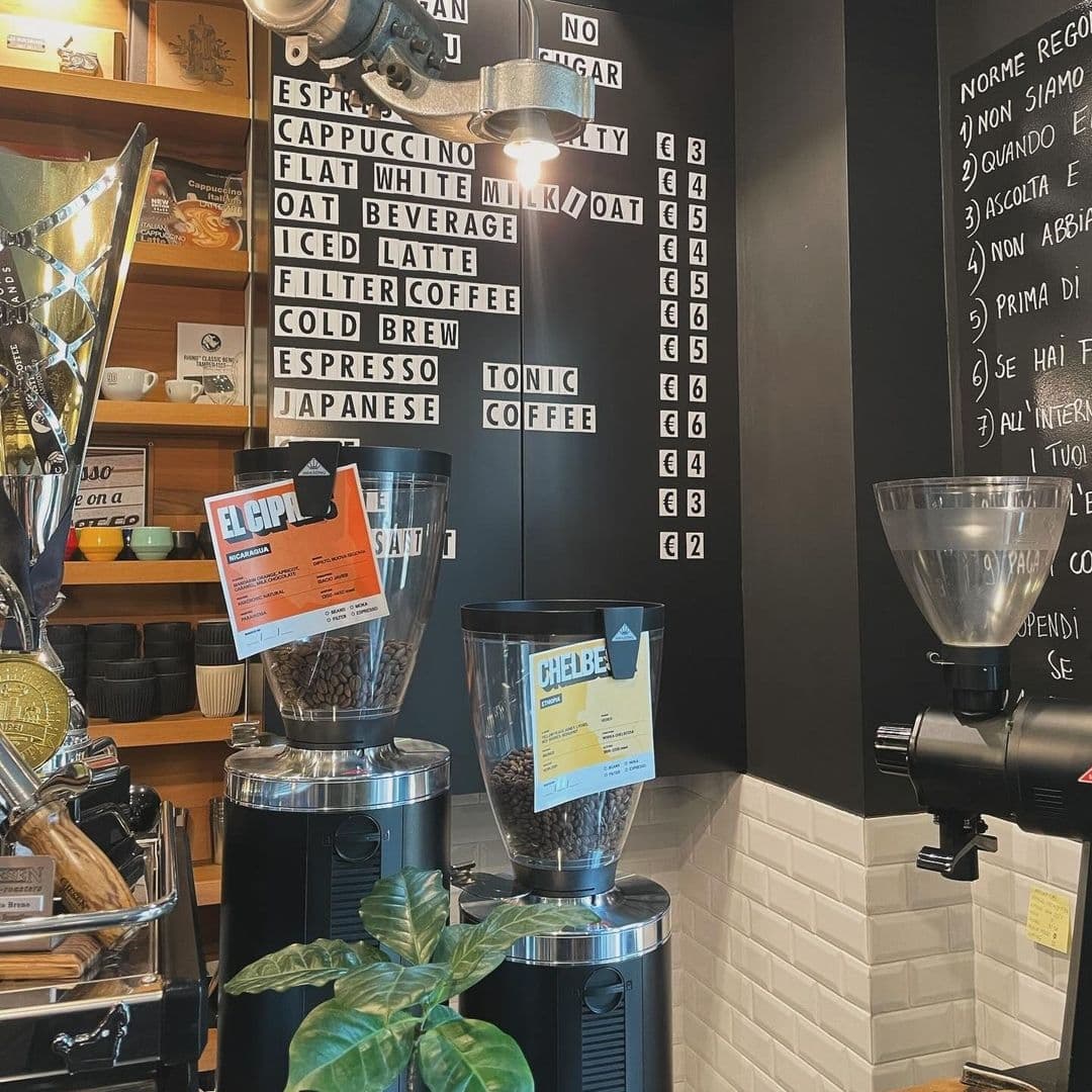 Interior view of Out of the Woods coffee shop with espresso machines, coffee beans in clear containers, and a menu board displaying various coffee options.