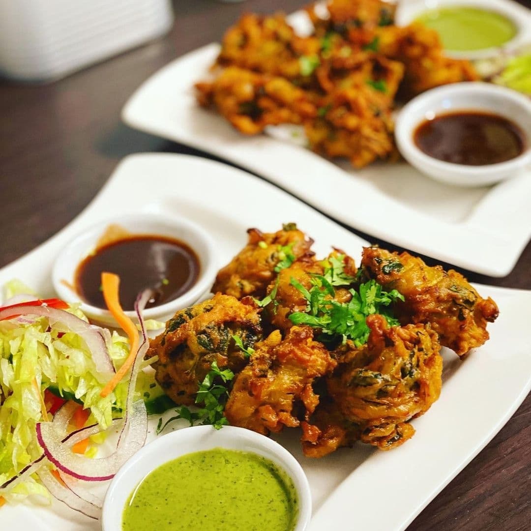 Delicious Indian appetizers at Rasoi Stories, featuring golden-brown pakoras garnished with fresh cilantro, served with green chutney and tamarind sauce, accompanied by a fresh side salad.