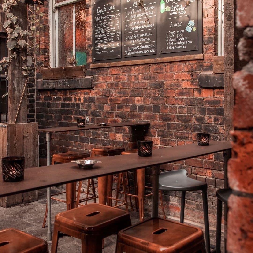 Interior of Roland's featuring rustic brick walls, wooden stools, and tables with candle holders, next to a chalkboard menu displaying drinks and snacks.
