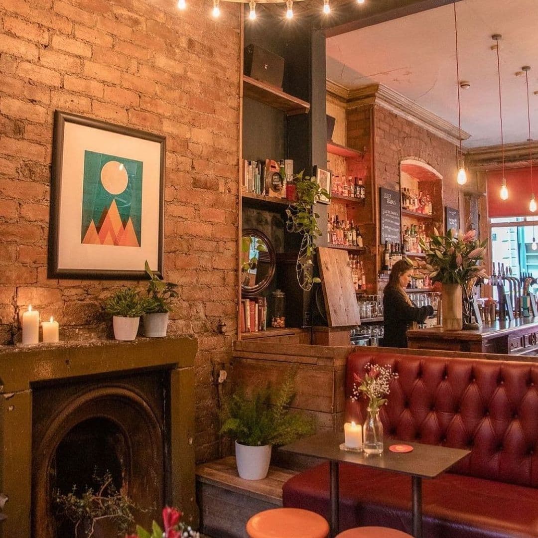 Interior of Roland's showing a cozy seating area with red leather booth, exposed brick walls, framed artwork, lit candles, and a bar counter with a bartender in the background.