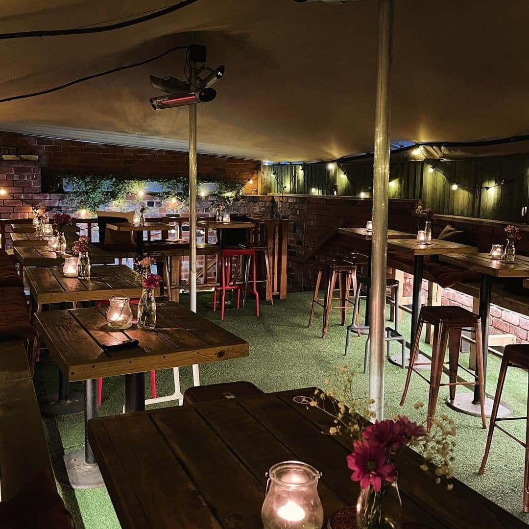 Cozy outdoor seating at Roland's with wooden tables, candlelit ambiance, and warm lighting under a canvas canopy.