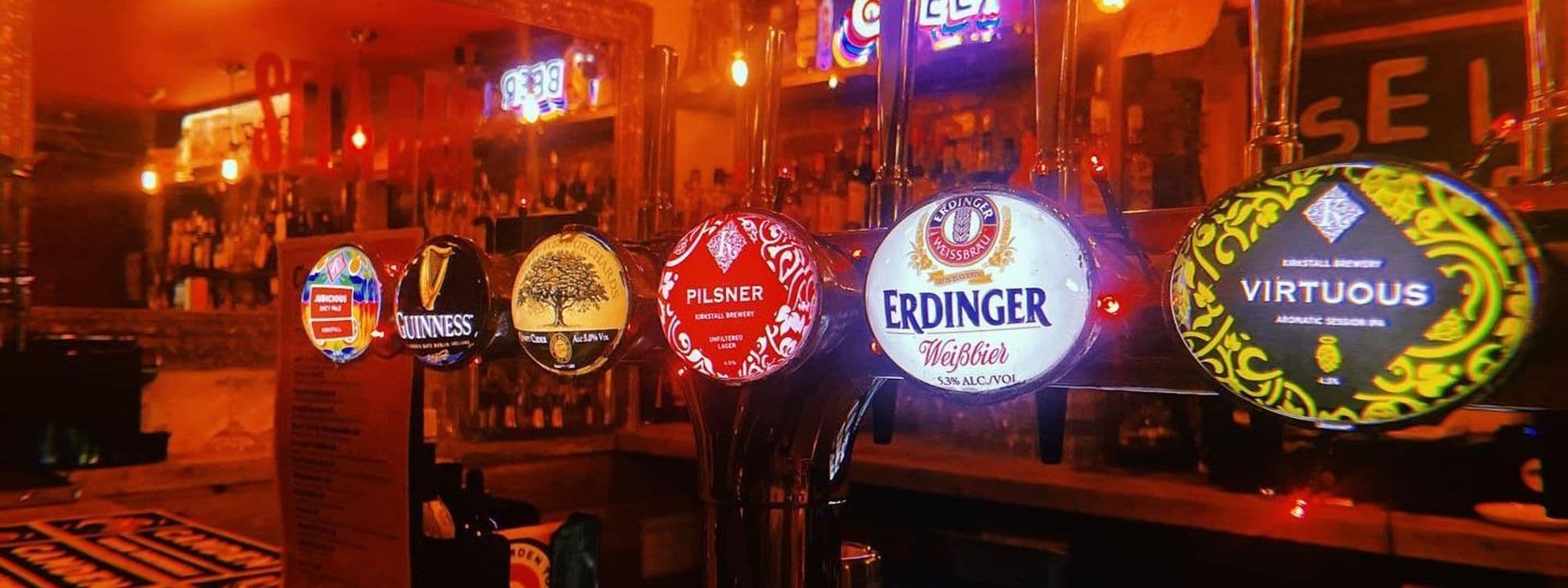 Close-up of a variety of beer taps at Sela Bar, featuring brands like Guinness and Erdinger, with a warm, inviting ambiance in the background.