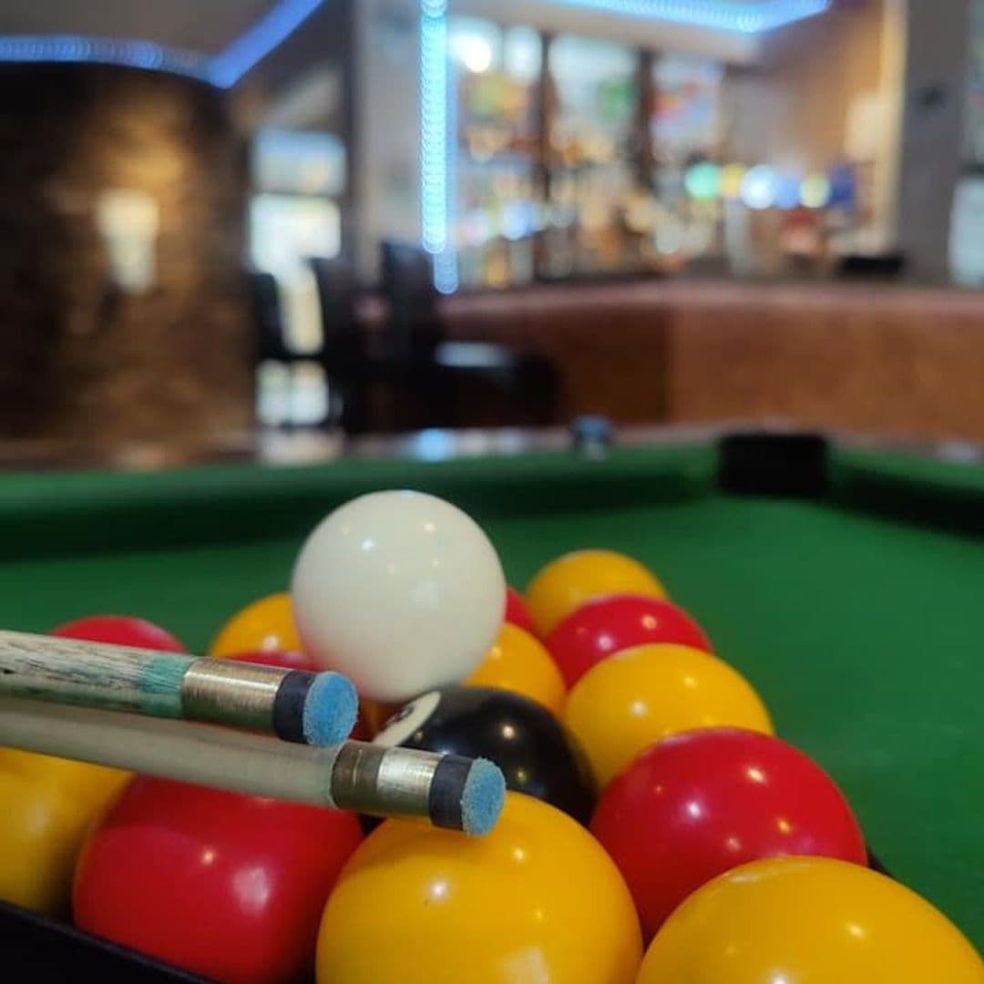 Close-up of a racked set of pool balls with cues ready for a game at The Grand Valley Bar & Kitchen, with a blurred background featuring the bar area.