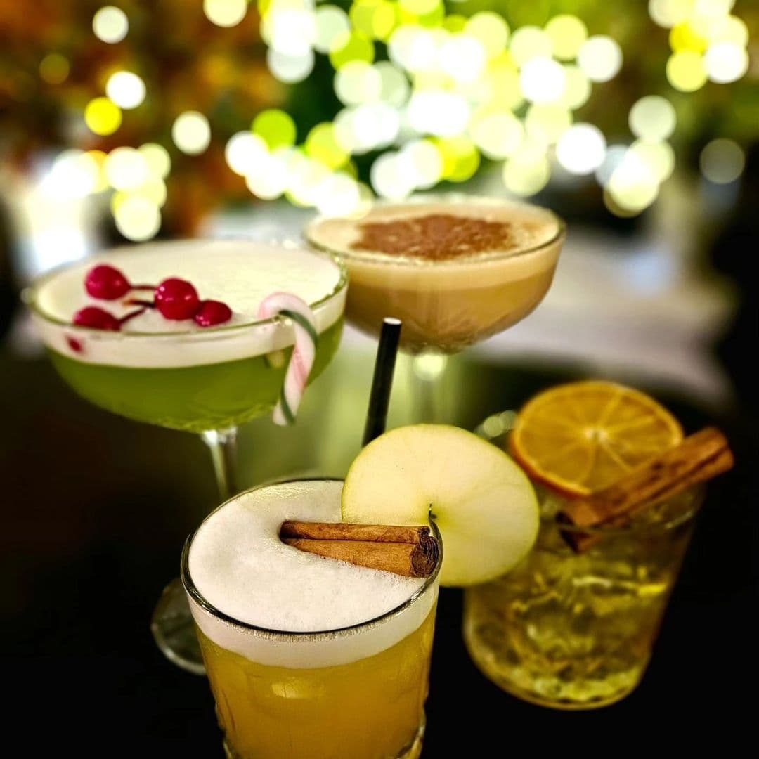 Assorted cocktails at The New Conservatory with festive garnishes, blurred lights in the background.