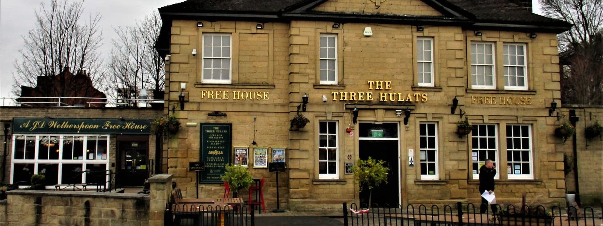 Exterior view of The Three Hulats, a traditional free house pub with a stone facade, large windows, and a signboard displaying the name in gold lettering.