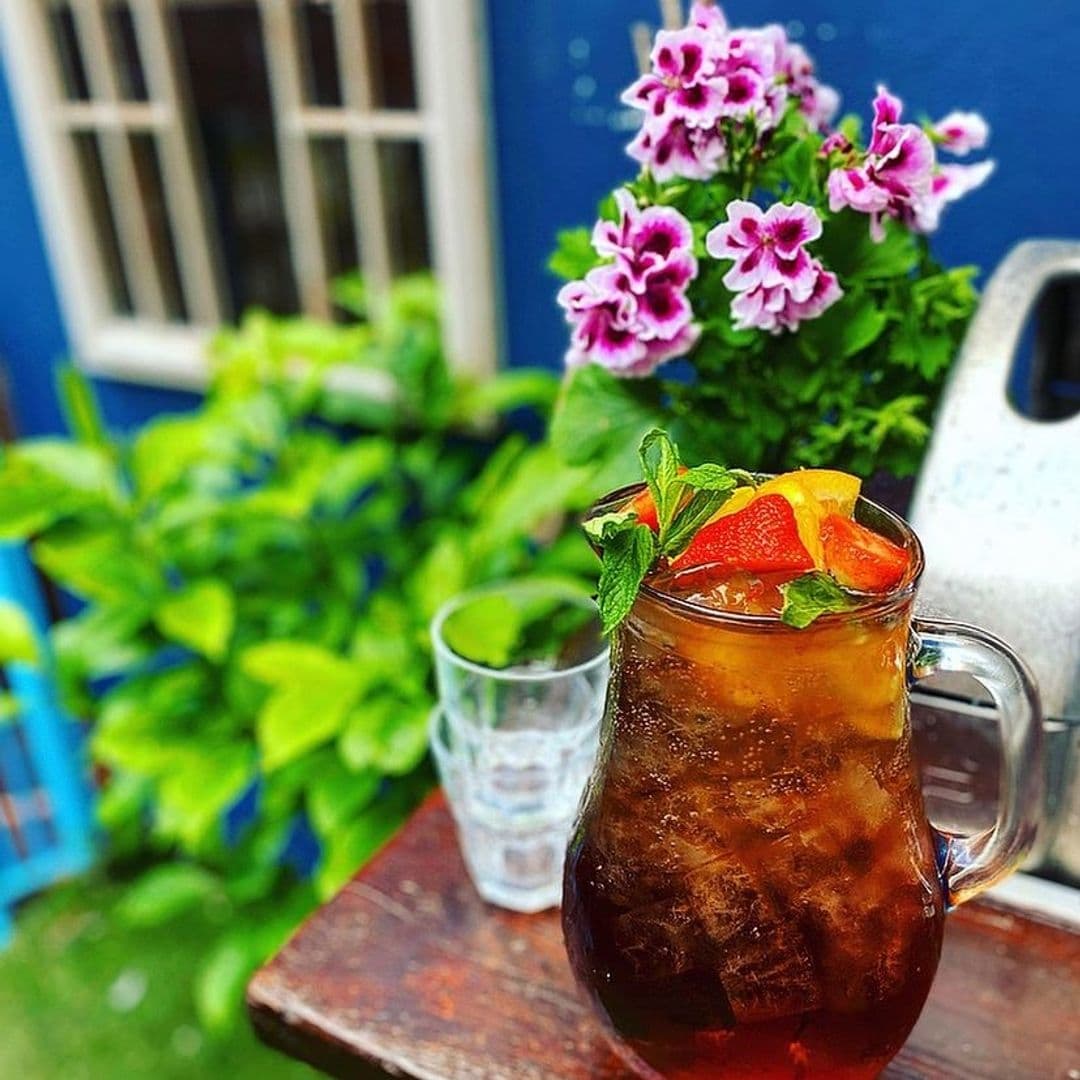 Refreshing iced drink garnished with mint and citrus at Cuckoo, with vibrant flowers and a blue window in the background.
