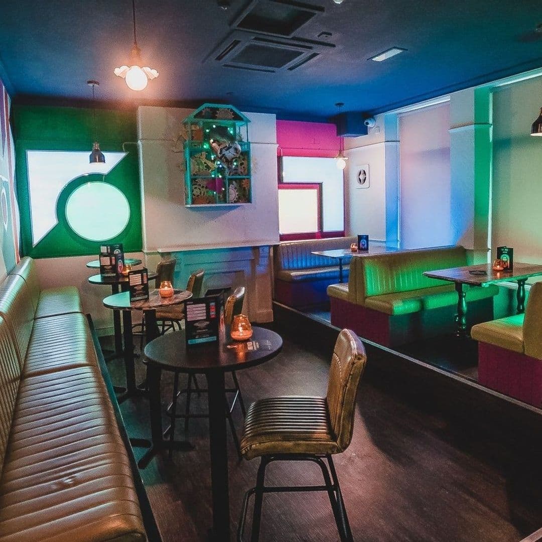 Interior of Cuckoo: a cozy bar with eclectic decor, featuring colorful lighting, a mix of booth and table seating, and quirky wall art.