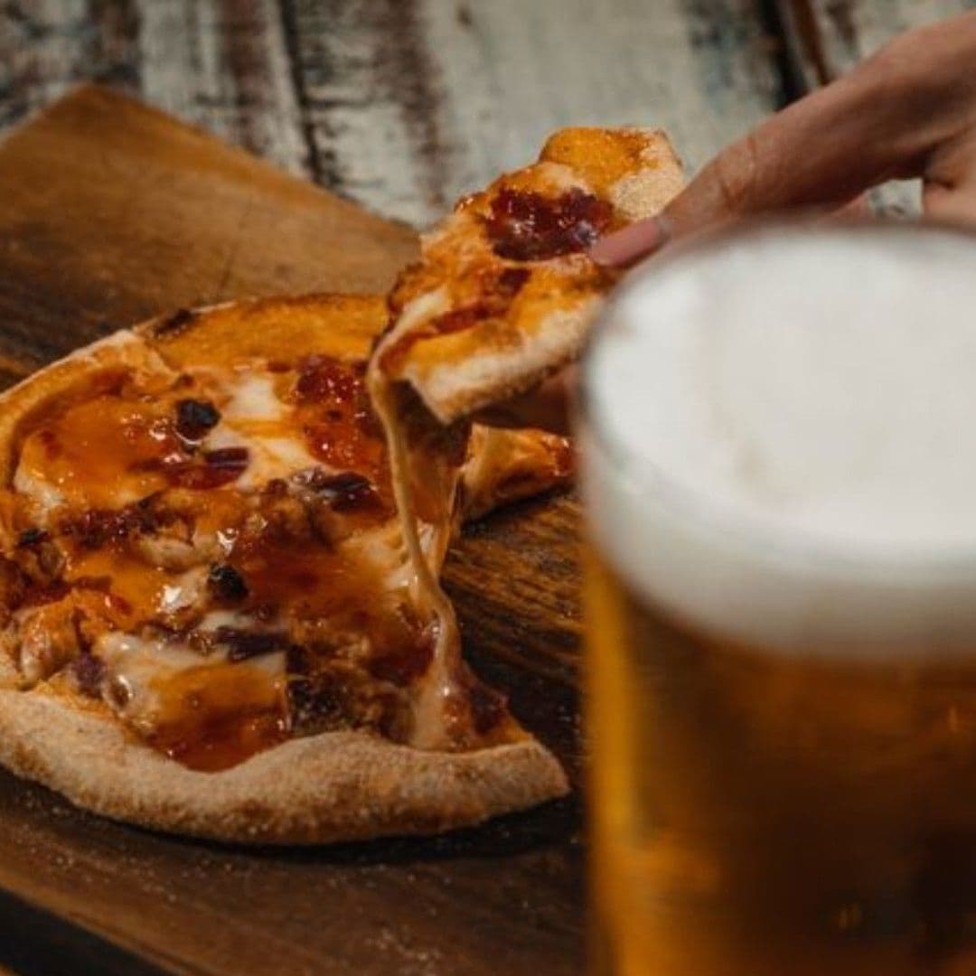 Alt text: "Delicious pizza with melted cheese being lifted from a wooden board, with a glass of frothy beer at Cuckoo."