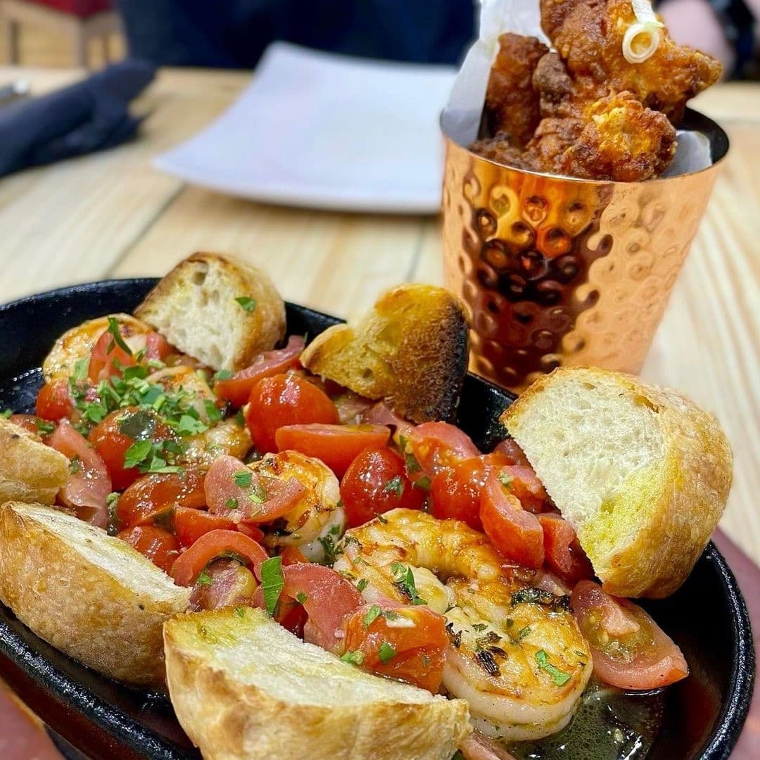 Sizzling shrimp and diced tomato appetizer with toasted bread, alongside a cup of crispy fried chicken pieces at Ecco Pizzeria.