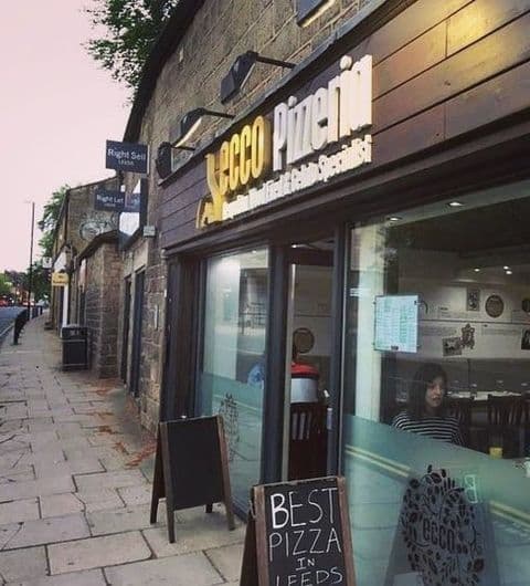 Exterior view of Ecco Pizzeria with signage, sidewalk, and a chalkboard advertising "BEST PIZZA IN LEEDS."