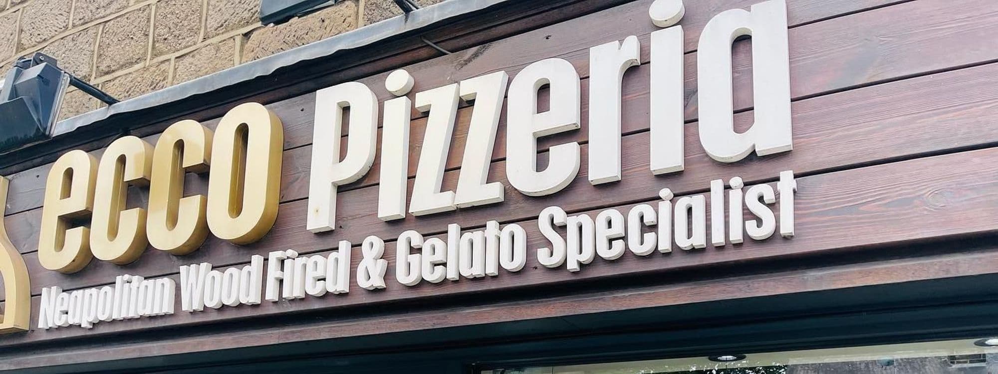 Signboard of Ecco Pizzeria featuring large, cream-colored letters against a dark wooden backdrop, advertising Neapolitan Wood Fired & Gelato Specialists.
