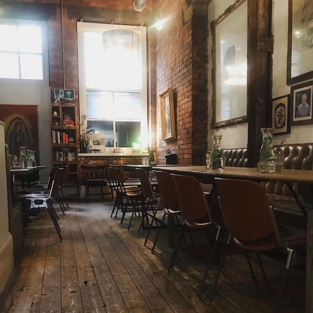 Interior of Mrs Atha's with vintage-style decor, exposed brick walls, wooden floors, and a cozy seating arrangement with brown chairs and a leather bench.