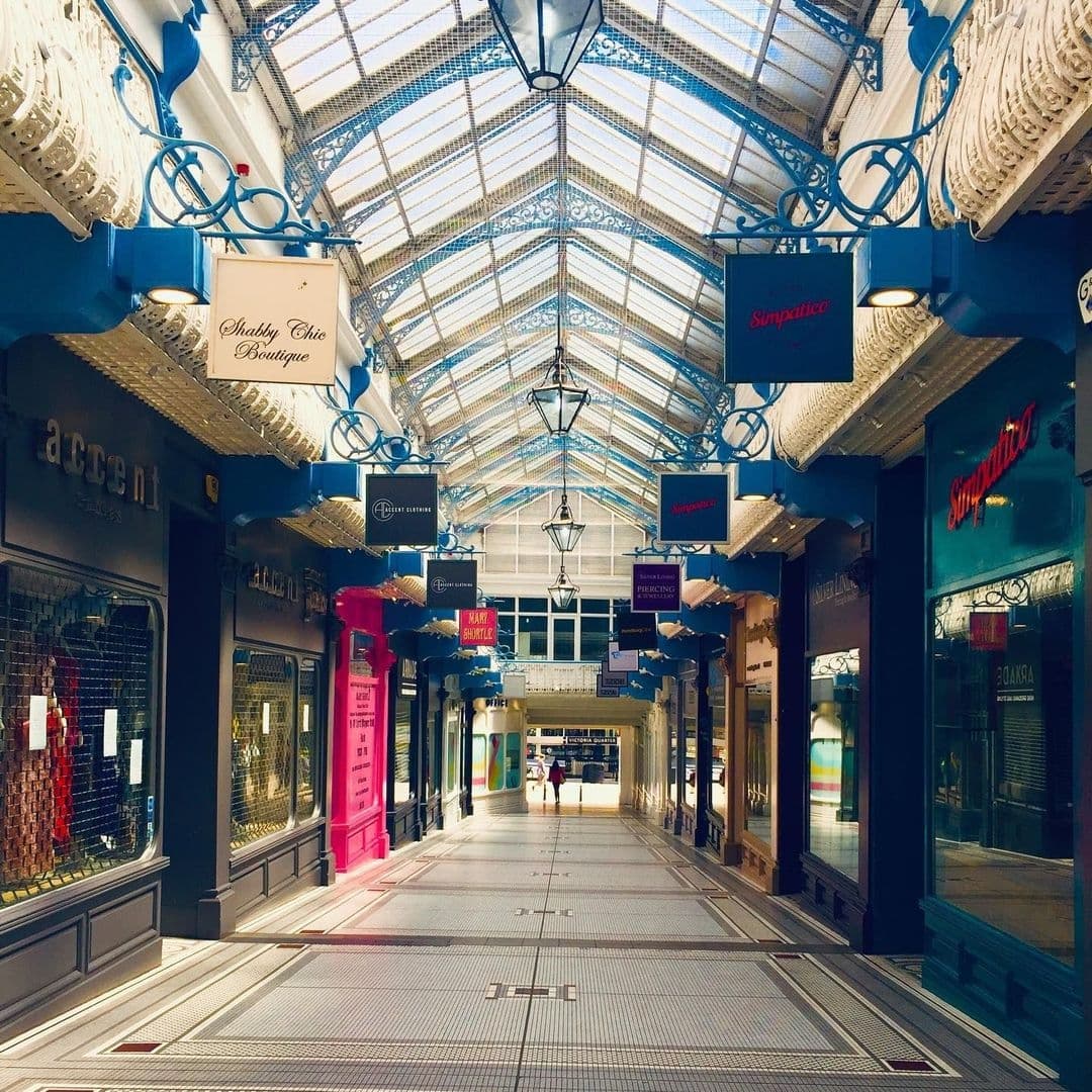Interior view of Olive & Rye shopping arcade with decorative hanging lights, glass roof, and lined with various boutique shops and colorful storefronts.