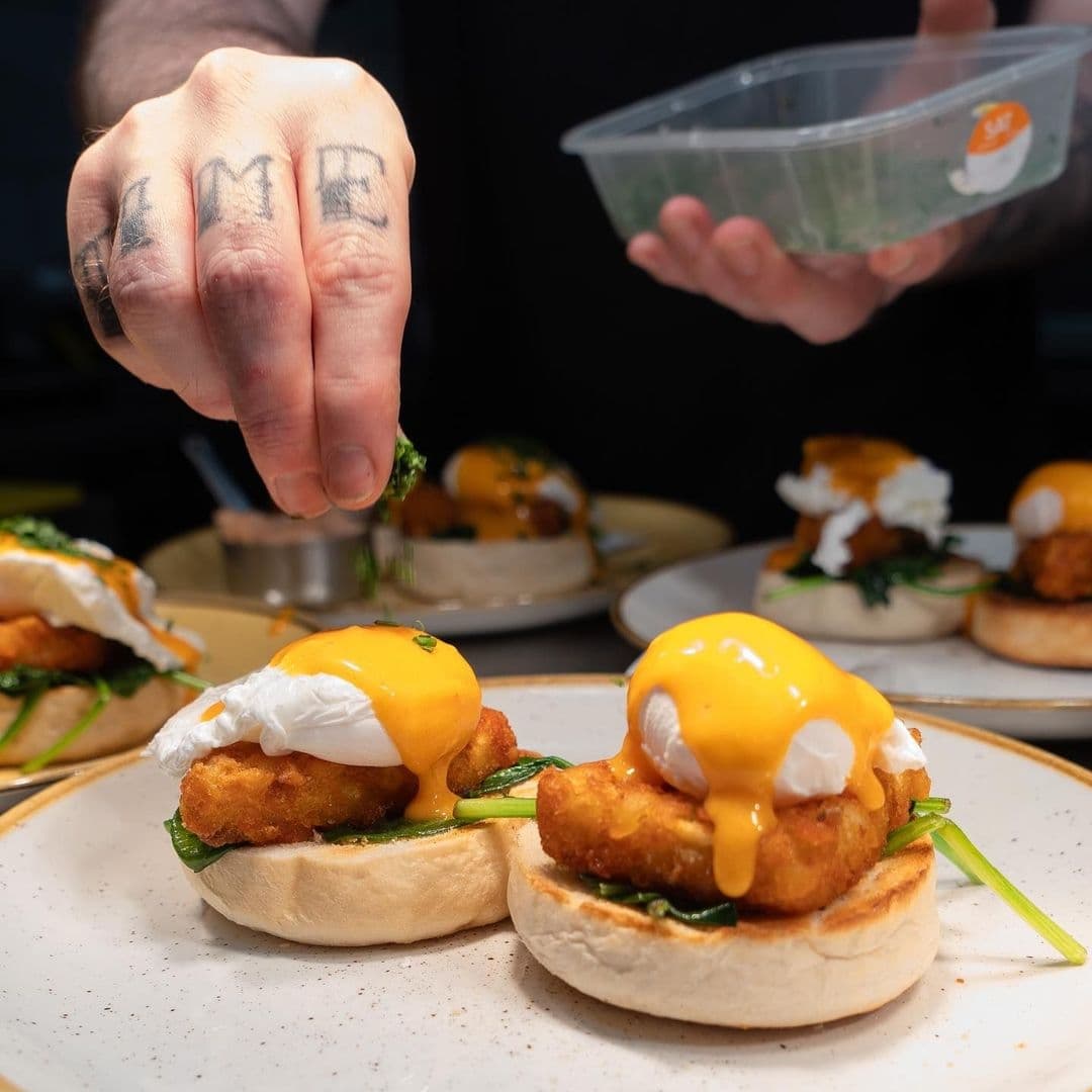 Close-up of a chef garnishing poached eggs on English muffins with hollandaise sauce at Olive & Rye.