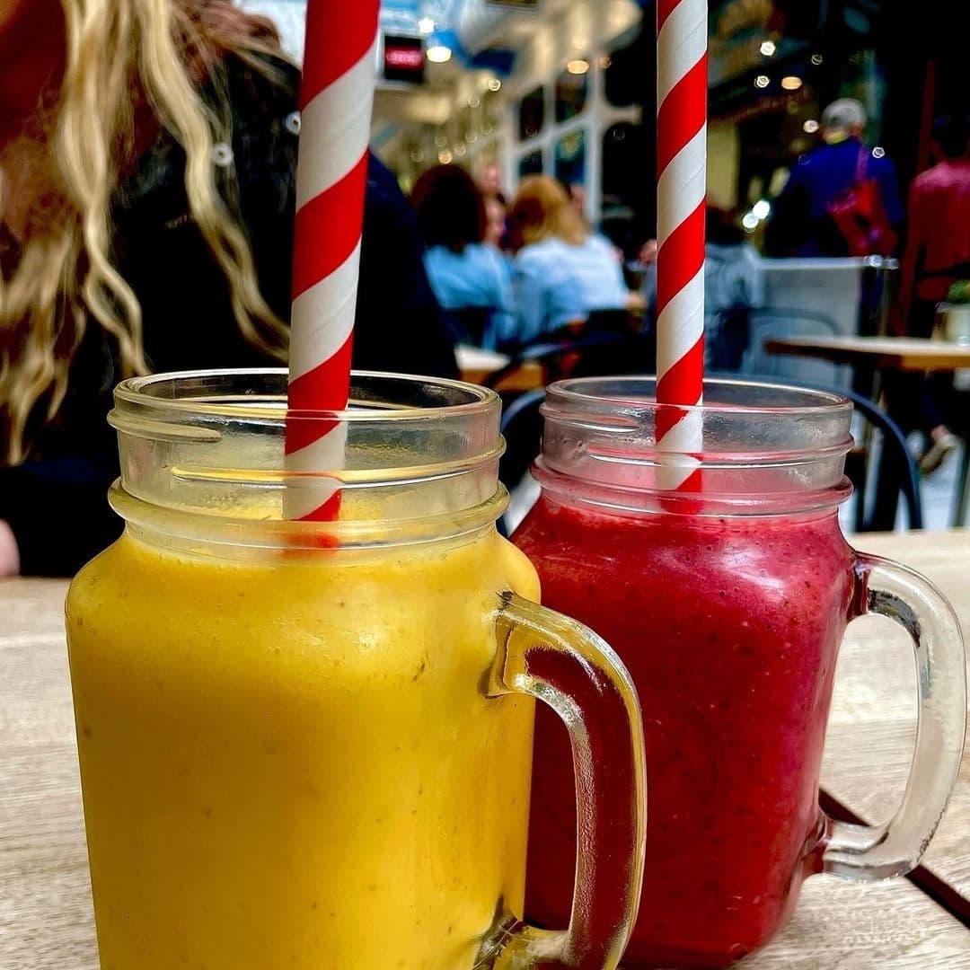 Two colorful smoothies in mason jars with red and white striped straws at Olive & Rye, with a blurred background of a cafe setting.