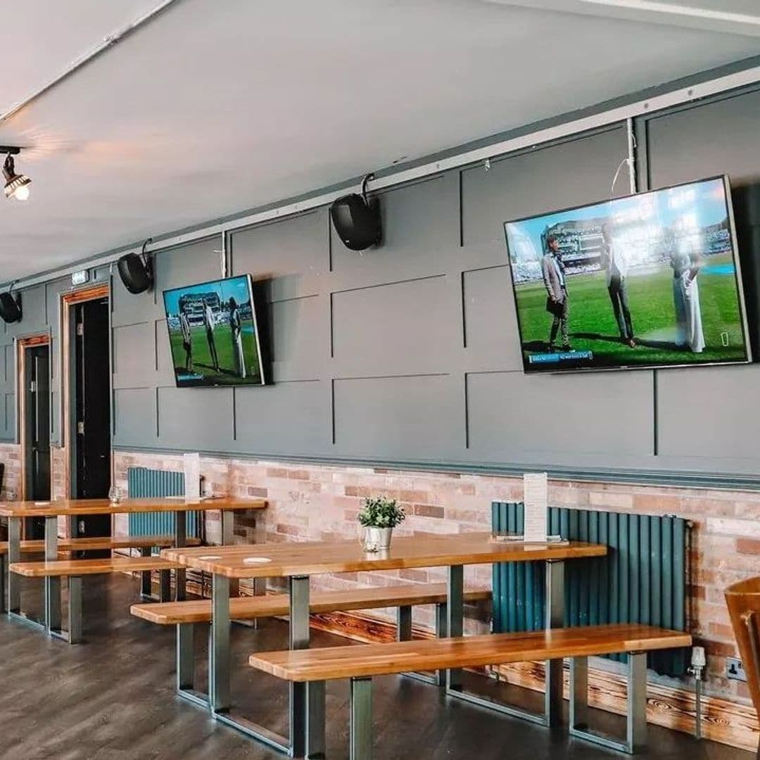 Interior of Parkside Tavern with wooden tables and benches, brick wall accents, and flat-screen TVs displaying sports.