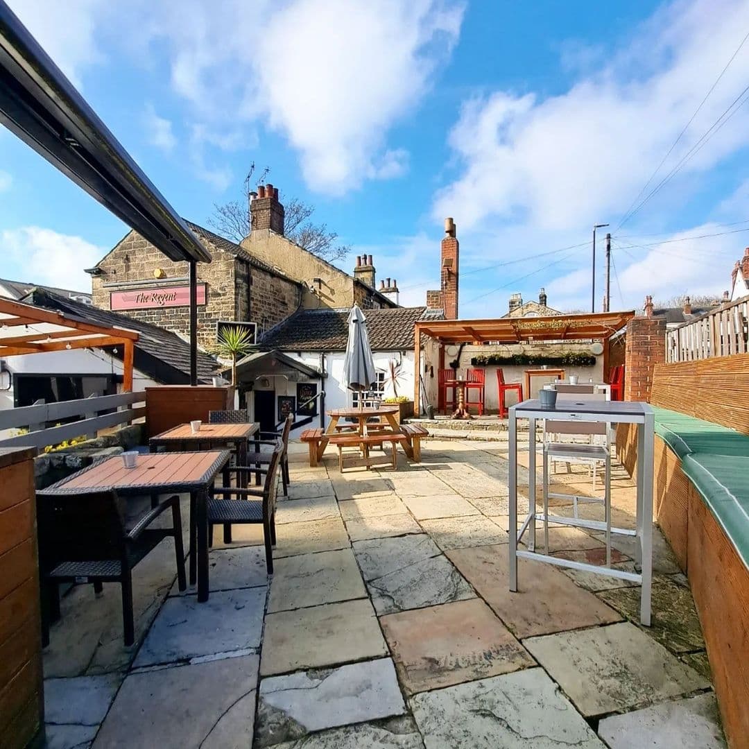 Outdoor seating area at Regent with various tables and chairs under a clear sky, adjacent to a building with a sign reading 'The Regent'.