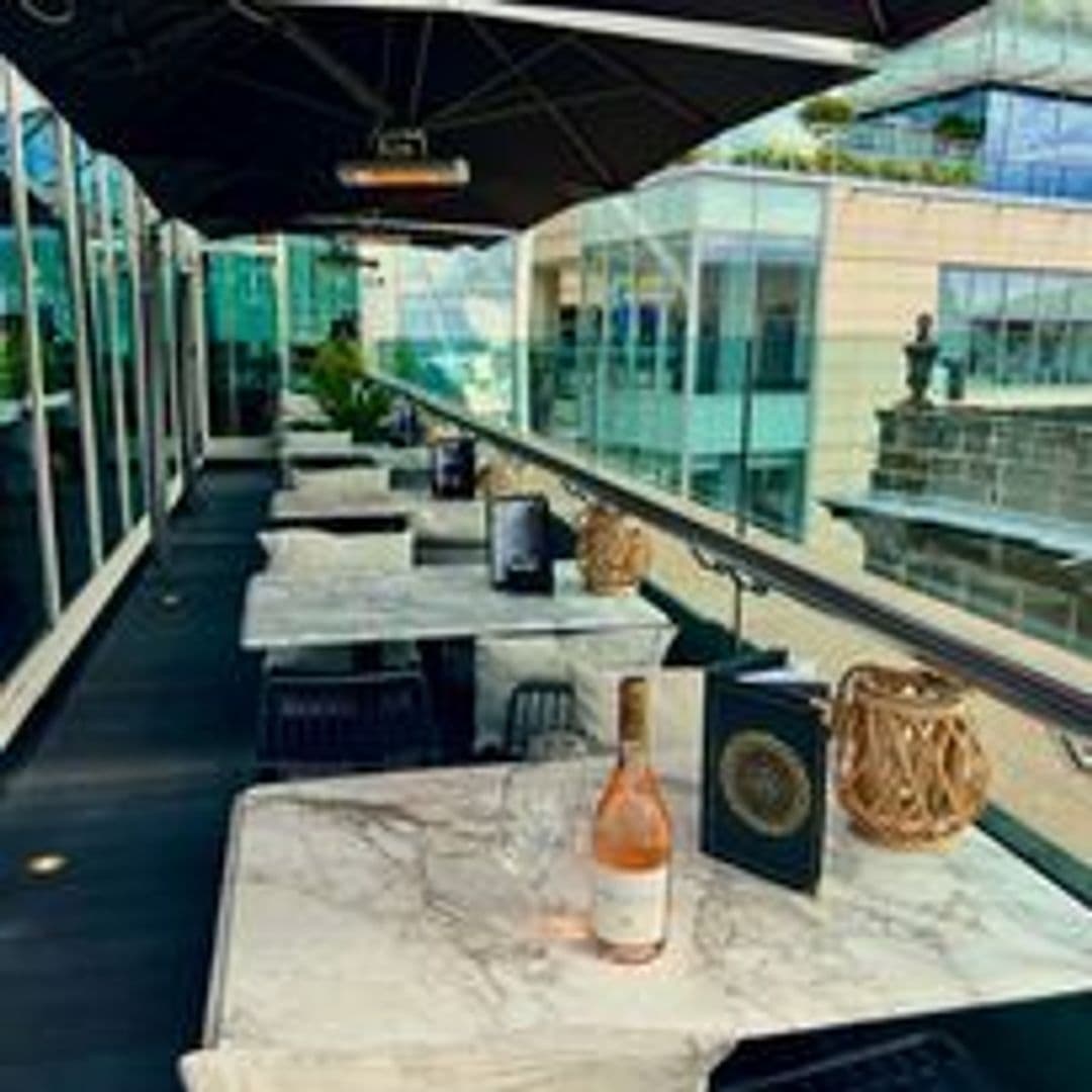Outdoor seating at The Alchemist Trinity with marble tables, a bottle of rosé wine, and a view of modern glass buildings.