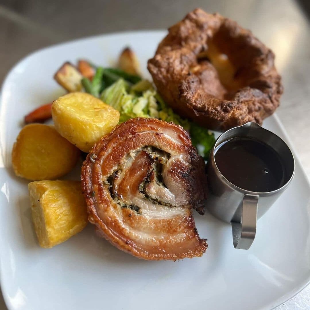 Traditional British Sunday roast with pork belly, roasted potatoes, a Yorkshire pudding, vegetables, and gravy at The Woods.
