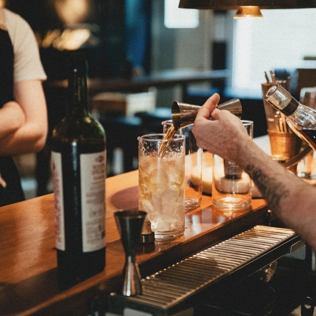 Bartender pouring a drink at Below Stairs, with wine bottle and bar equipment in view.