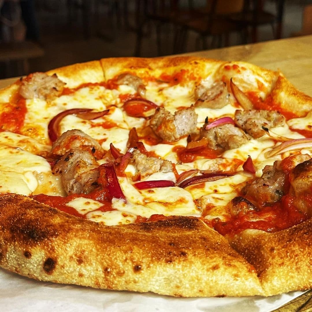 Freshly baked pizza with toppings of sausage, red onions, and bell peppers at Canteen.