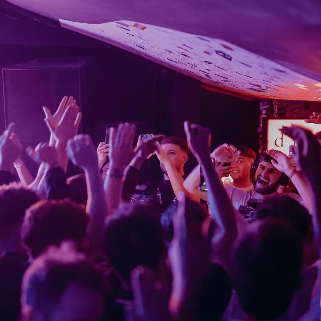 Excited crowd enjoying a vibrant nightlife scene at Distrikt, with people raising their hands in the air and some capturing the moment on their phones.