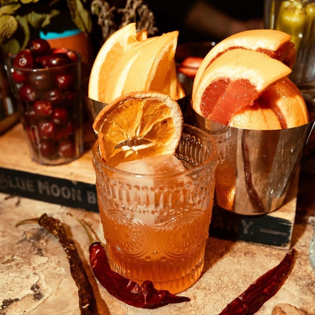 Close-up of a crafted cocktail with citrus garnishes at Distrikt, surrounded by fresh fruits and spices on a rustic table.