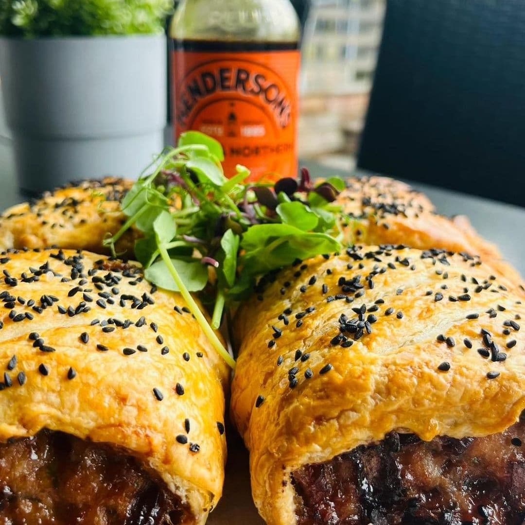 Savory puff pastry with meat filling and black sesame seeds on top, served with fresh greens, at Gray's restaurant. A bottle of Henderson's sauce is visible in the background.