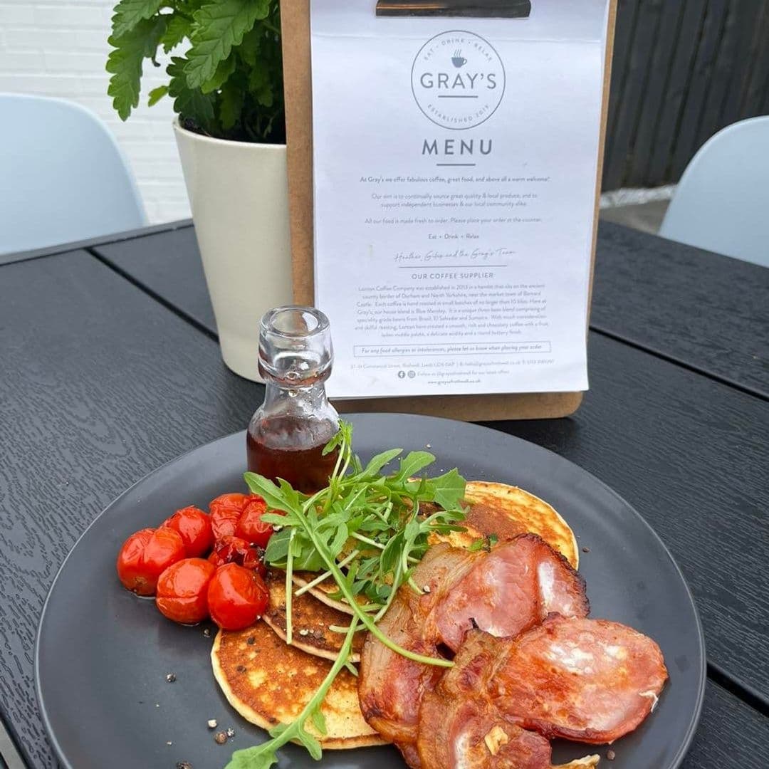 Alt text: "Delicious breakfast at Gray's featuring pancakes with syrup, crispy bacon, roasted tomatoes, and fresh arugula, served on a black plate with Gray's menu visible in the background."