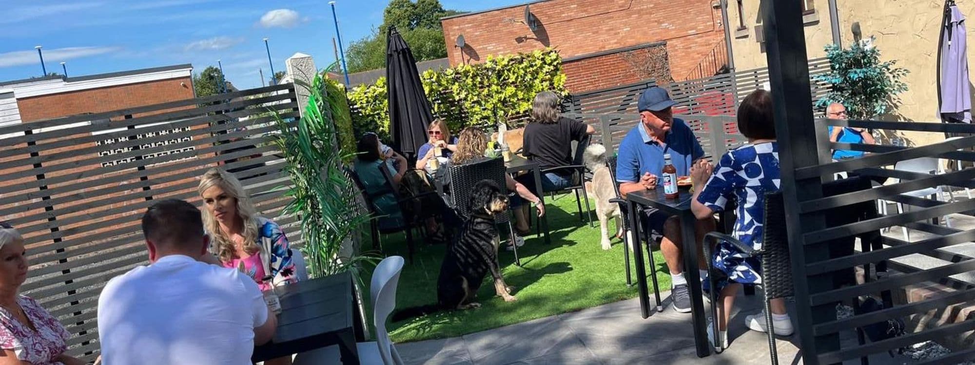 Outdoor seating area at Gray's with guests enjoying drinks and conversation on a sunny day, featuring green plants and umbrellas for shade.