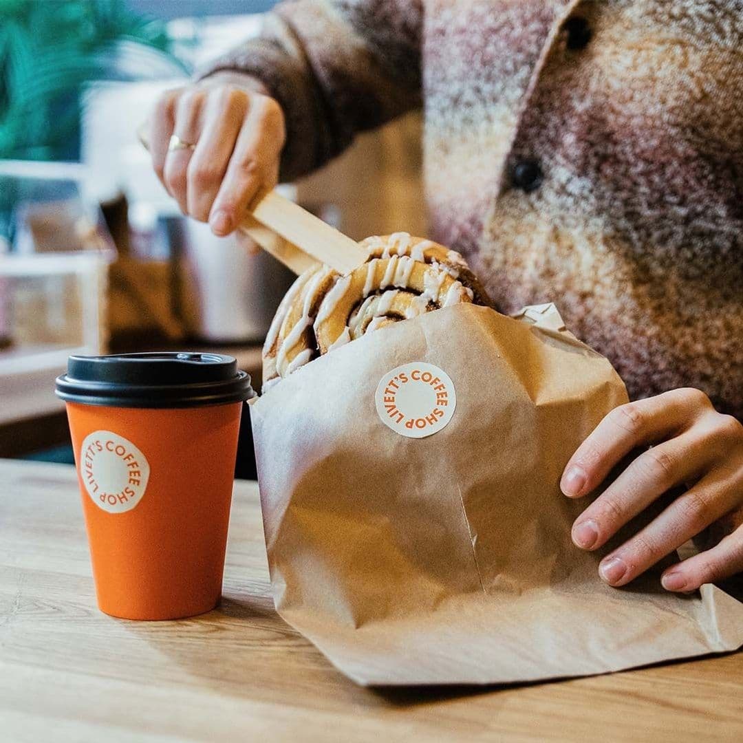 Person enjoying a cinnamon roll and takeaway coffee from Livett's Coffee Shop.