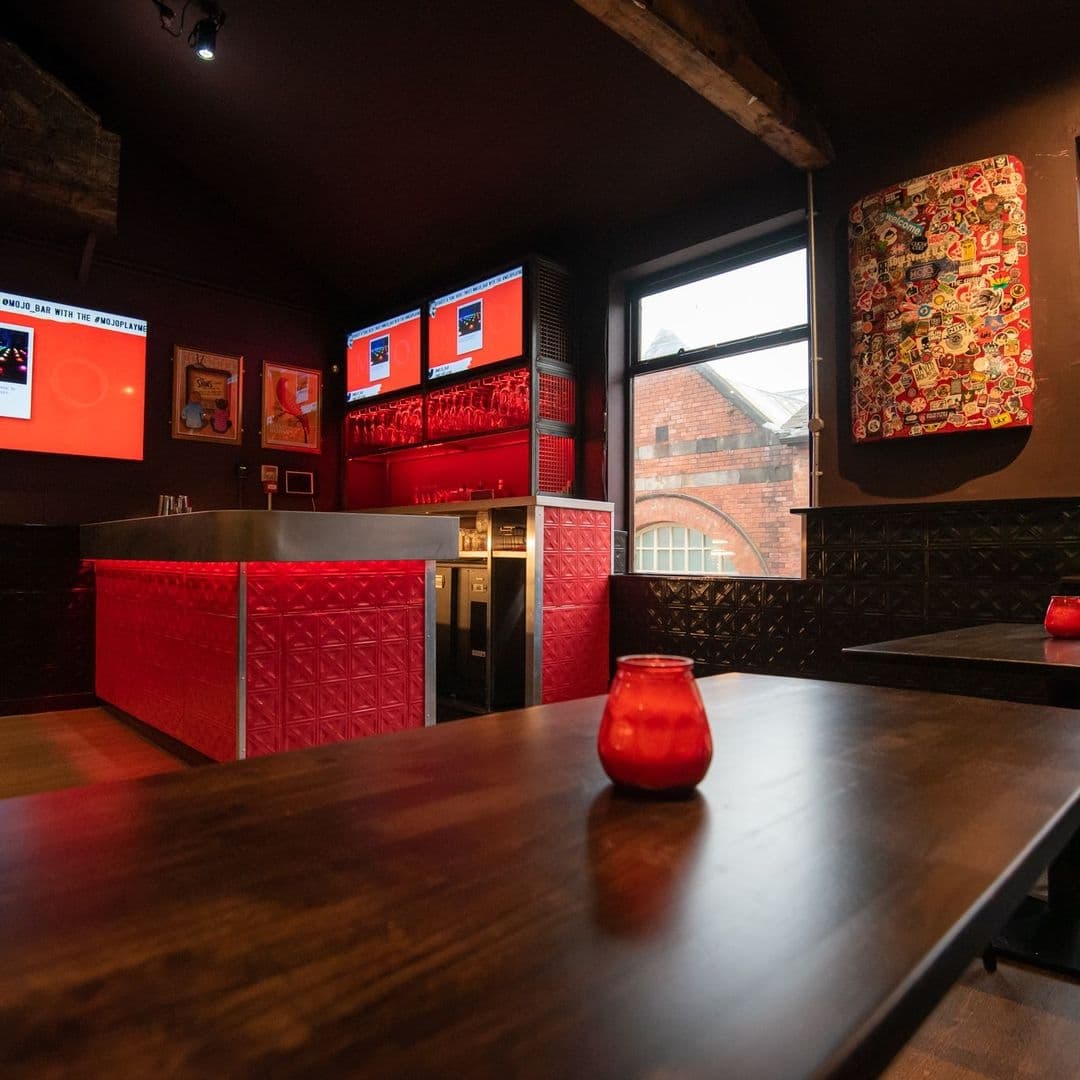 Interior of MOJO bar with red accent lighting, patterned wall panels, and decorative artwork, showcasing a relaxed and stylish atmosphere.