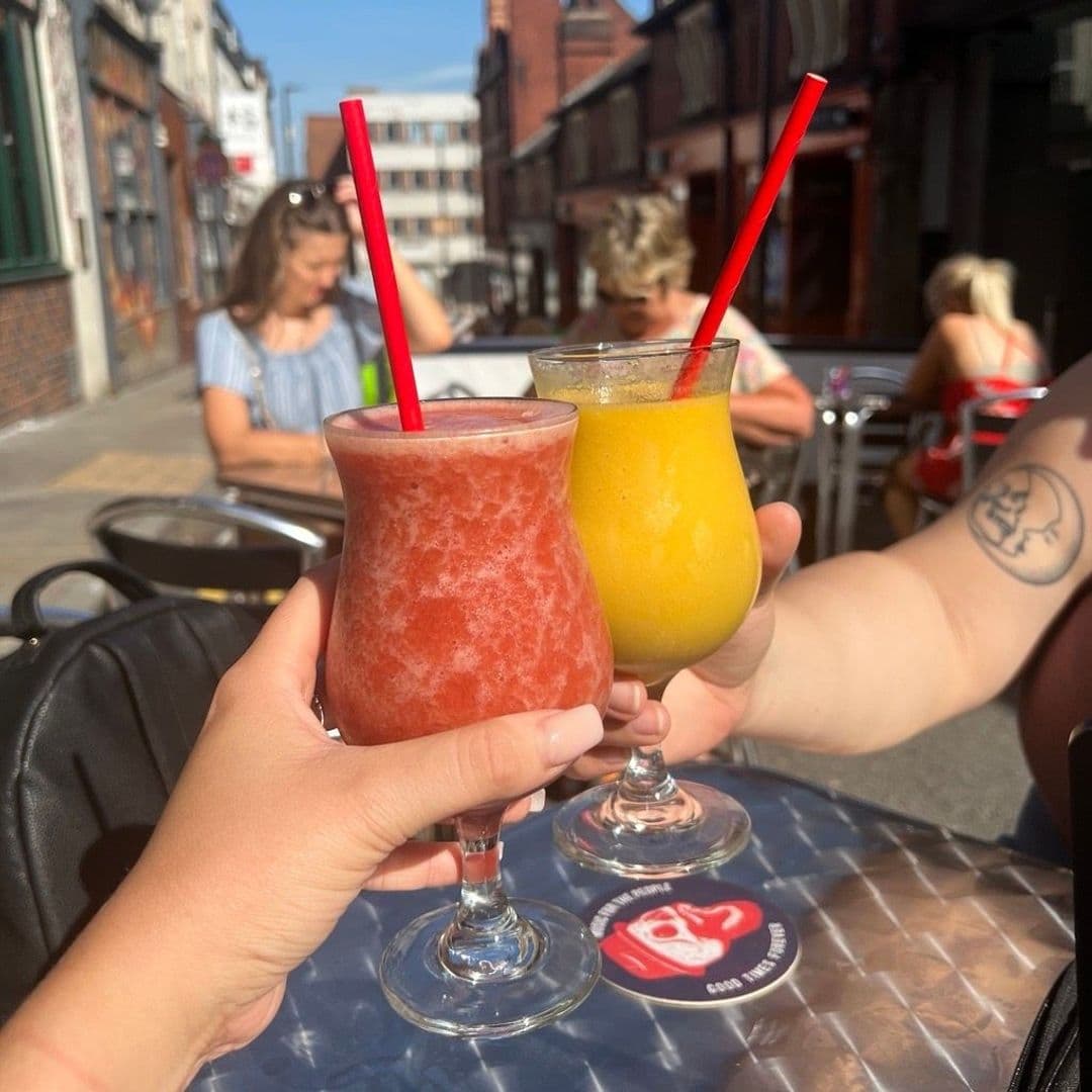 Two people enjoying refreshing frozen cocktails at MOJO, with a vibrant street scene in the background.