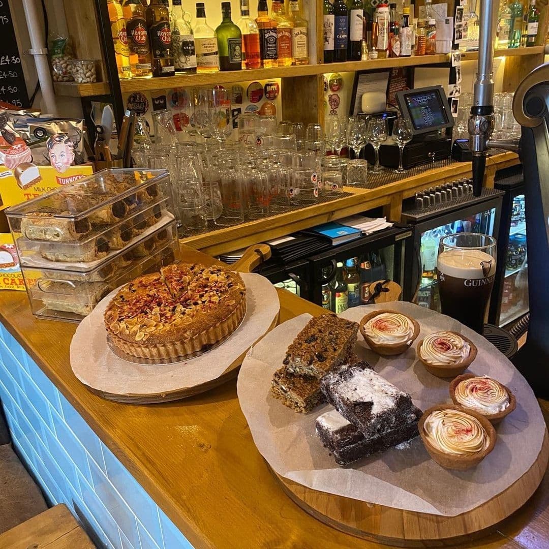 Assorted freshly baked pastries and desserts displayed on a wooden counter at Melodie 71, with a cozy bar background featuring a variety of beverages and a pint of Guinness.