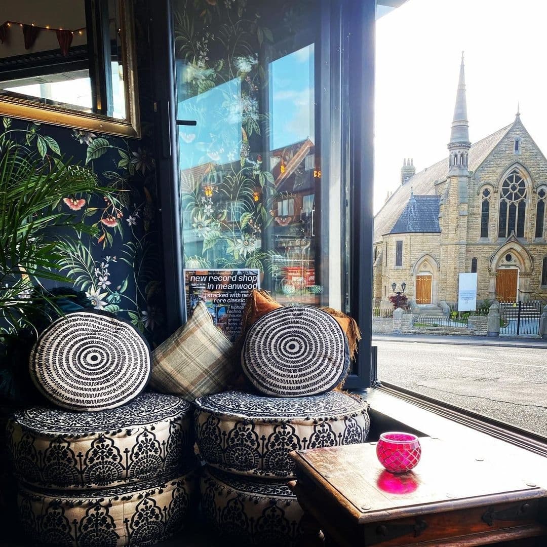 Interior view from Number 8 featuring patterned cushions on decorative stools near a window, with a view of a historic stone church across the street, reflecting the local charm and inviting atmosphere.